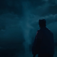A man in a baseball cap watches an unnatural column of clouds rise into the night sky.
